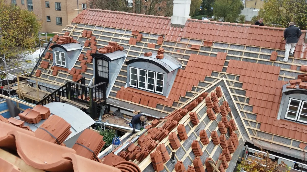 Tegltag under udskiftning på historisk ejendom, med nye tegl stablet på friske lægter og dormer-kviste under renovering.
